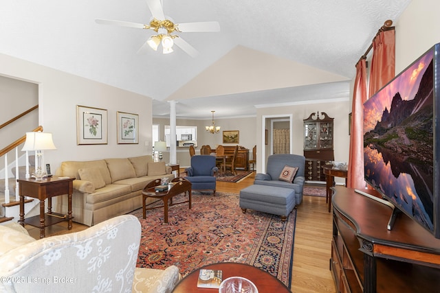 living room featuring light wood-type flooring, ceiling fan with notable chandelier, lofted ceiling, stairs, and ornate columns