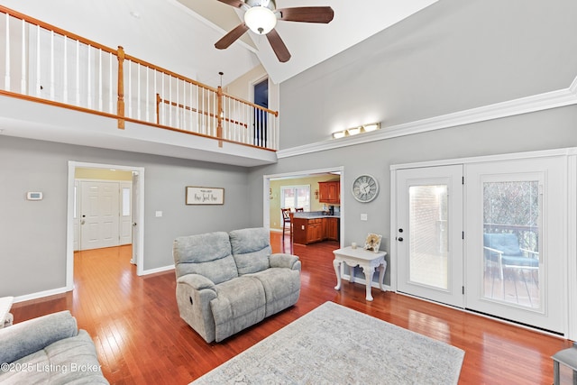 living area with ceiling fan, wood-type flooring, a towering ceiling, and baseboards