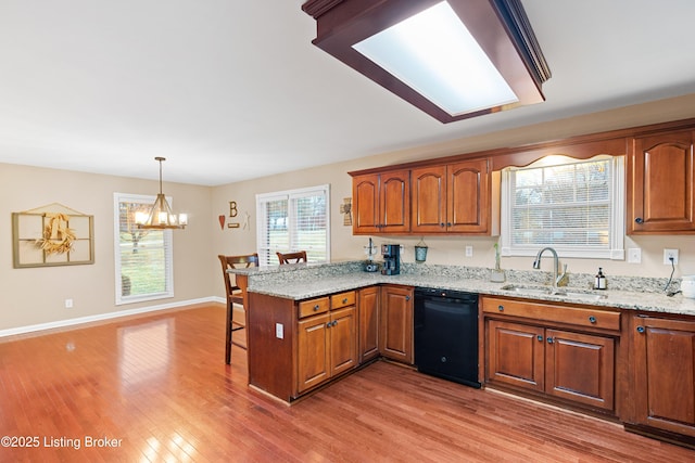 kitchen featuring a breakfast bar area, light wood-style flooring, a sink, dishwasher, and a peninsula