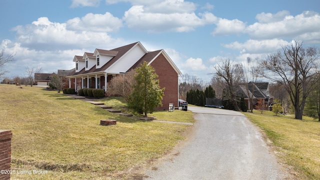 view of side of home featuring gravel driveway, a lawn, and brick siding