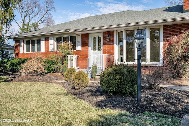 view of front of property with brick siding, roof with shingles, and a front lawn