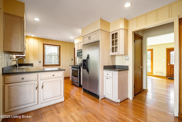 kitchen featuring light wood finished floors, stainless steel appliances, recessed lighting, glass insert cabinets, and a sink