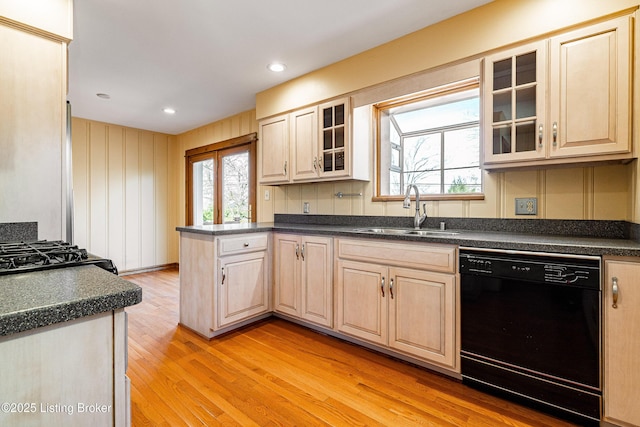 kitchen with dark countertops, a sink, light wood-type flooring, dishwasher, and a peninsula