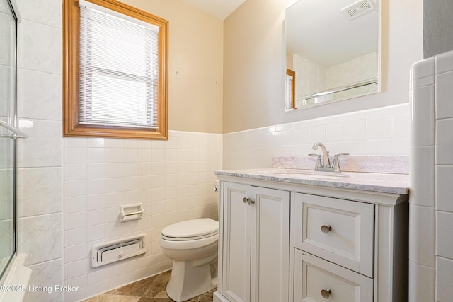 bathroom featuring visible vents, toilet, a shower with shower door, vanity, and tile walls