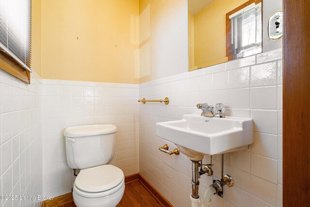 bathroom with toilet, a wainscoted wall, tile walls, and wood finished floors