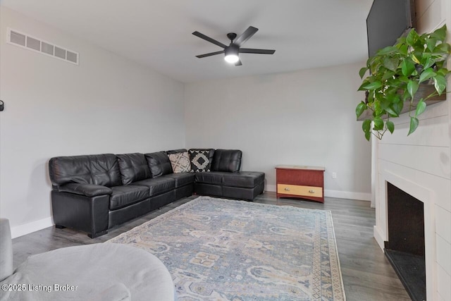 living room with baseboards, visible vents, a ceiling fan, wood finished floors, and a fireplace