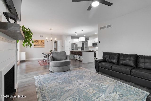 living room with ceiling fan with notable chandelier, wood finished floors, visible vents, and baseboards