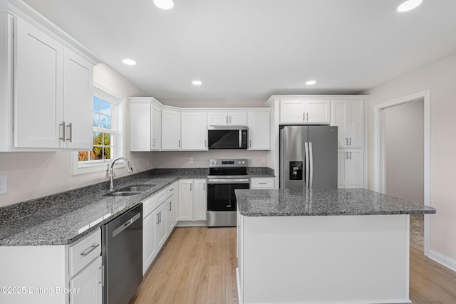 kitchen with stainless steel appliances, a sink, white cabinets, a center island, and dark stone counters