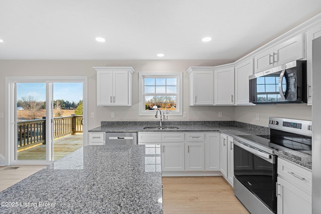 kitchen featuring stainless steel appliances, white cabinetry, a sink, light wood-type flooring, and dark stone counters