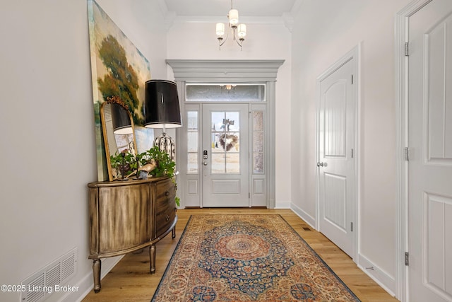 entryway with light wood finished floors, visible vents, ornamental molding, a chandelier, and baseboards