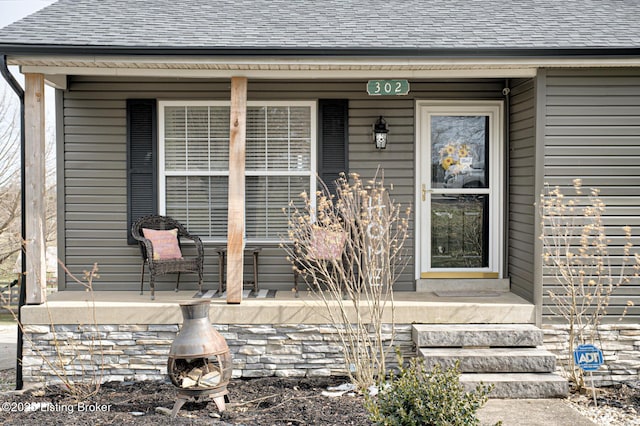 entrance to property featuring a porch and roof with shingles