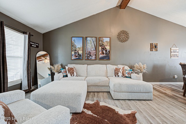 living room featuring lofted ceiling with beams, light wood-style floors, and baseboards