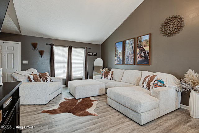 living room featuring vaulted ceiling, a textured ceiling, light wood-style flooring, and baseboards