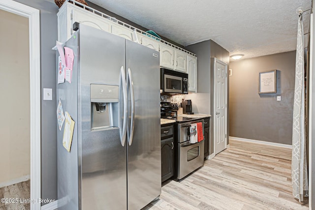 kitchen featuring light wood finished floors, appliances with stainless steel finishes, a textured ceiling, white cabinetry, and backsplash