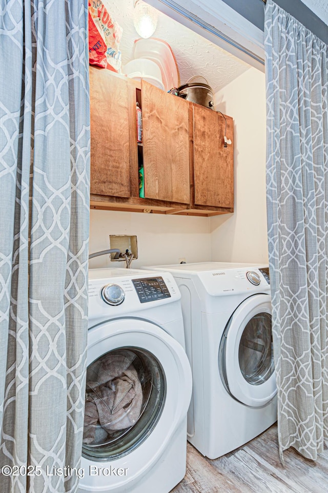 clothes washing area featuring washing machine and dryer, cabinet space, and light wood finished floors