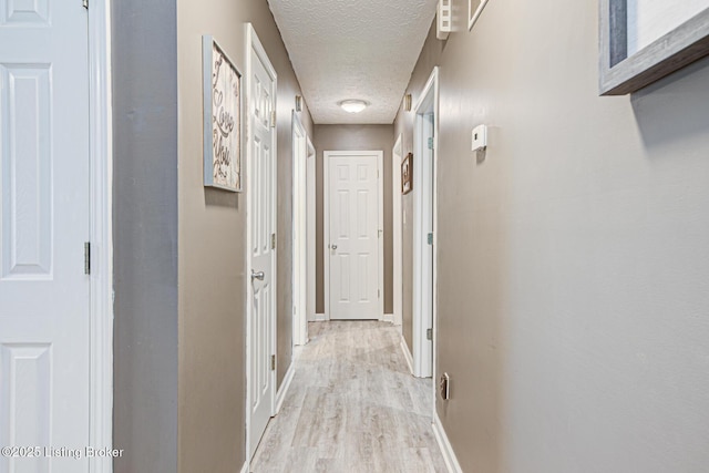 corridor with light wood-style floors, baseboards, and a textured ceiling