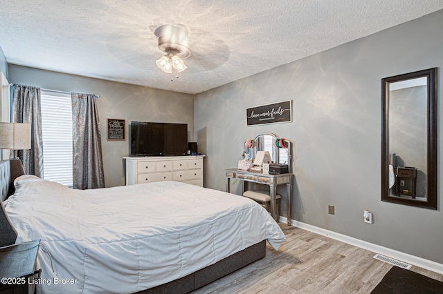 bedroom featuring visible vents, light wood-style floors, a ceiling fan, a textured ceiling, and baseboards