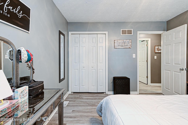 bedroom featuring a closet, visible vents, light wood-style floors, a textured ceiling, and baseboards