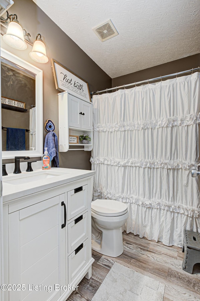 bathroom with visible vents, toilet, vanity, a textured ceiling, and wood finished floors