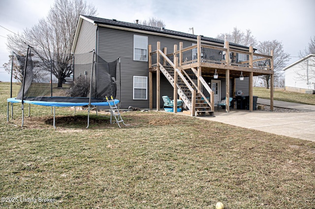 rear view of house with a patio, stairs, a lawn, a wooden deck, and a trampoline