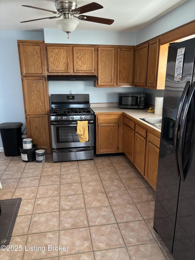 kitchen with stainless steel gas range oven, black fridge with ice dispenser, brown cabinets, light countertops, and light tile patterned flooring