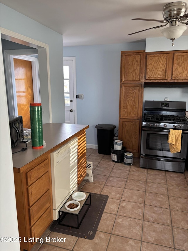 kitchen with brown cabinetry, gas range, a wood stove, white dishwasher, and light countertops