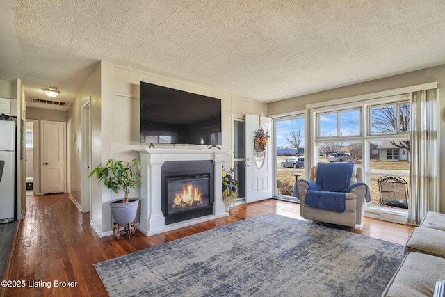 living room with a textured ceiling, wood finished floors, visible vents, baseboards, and a glass covered fireplace