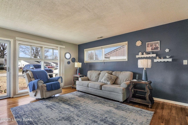 living area featuring visible vents, a textured ceiling, baseboards, and wood finished floors