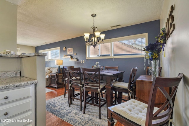 dining room featuring a notable chandelier, a textured ceiling, visible vents, and wood finished floors