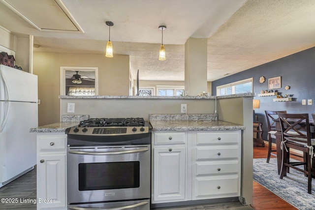 kitchen with stainless steel gas stove, white cabinets, dark wood finished floors, decorative light fixtures, and freestanding refrigerator