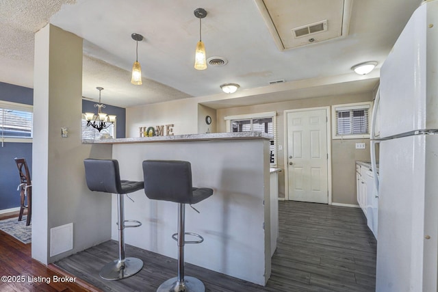 kitchen with visible vents, dark wood-type flooring, a breakfast bar area, and freestanding refrigerator