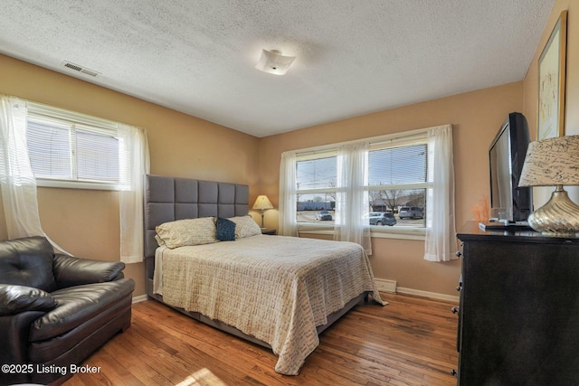 bedroom featuring baseboards, a textured ceiling, visible vents, and wood finished floors