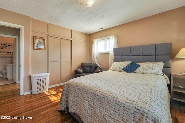 bedroom featuring a closet, visible vents, a textured ceiling, and wood finished floors