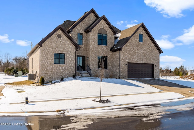 view of front facade with an attached garage, driveway, central air condition unit, and brick siding