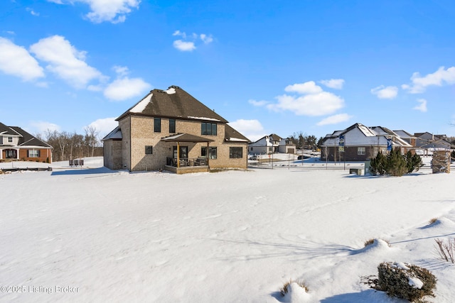 snow covered rear of property featuring a residential view and brick siding