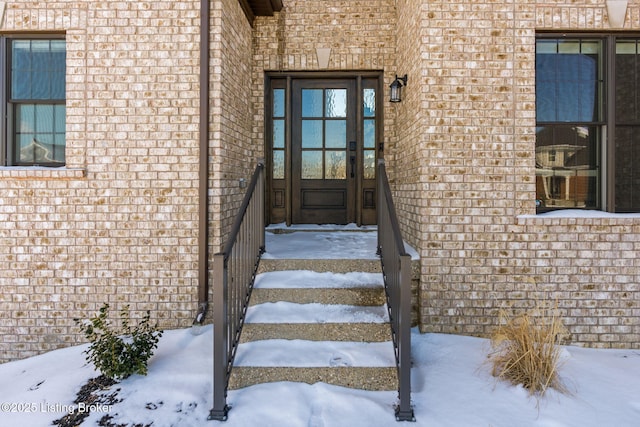 snow covered property entrance featuring brick siding