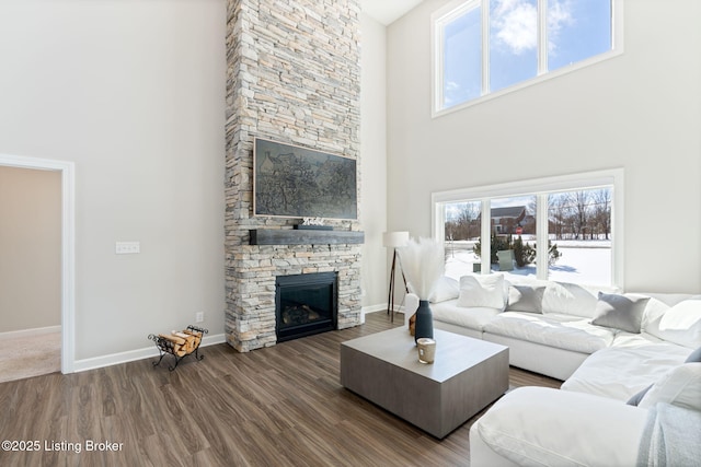 living room with a healthy amount of sunlight, a stone fireplace, baseboards, and wood finished floors