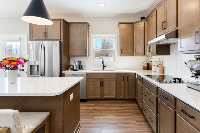 kitchen featuring brown cabinetry, appliances with stainless steel finishes, light countertops, under cabinet range hood, and a sink