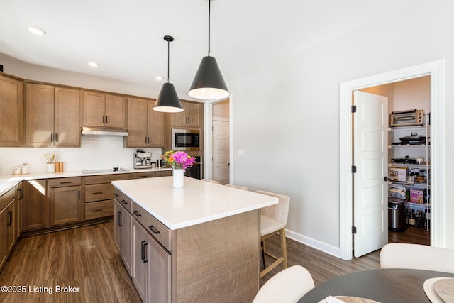 kitchen with a kitchen island, decorative light fixtures, built in microwave, light countertops, and under cabinet range hood