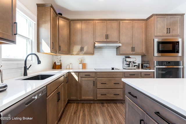 kitchen with under cabinet range hood, stainless steel appliances, a sink, and light countertops