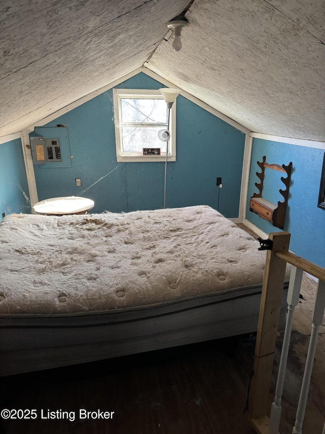 unfurnished bedroom featuring lofted ceiling, a textured ceiling, wood finished floors, electric panel, and track lighting