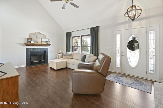 living room featuring dark wood-style flooring, a fireplace, high vaulted ceiling, baseboards, and ceiling fan with notable chandelier