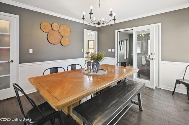 dining space featuring ornamental molding, dark wood-style flooring, a wainscoted wall, and an inviting chandelier