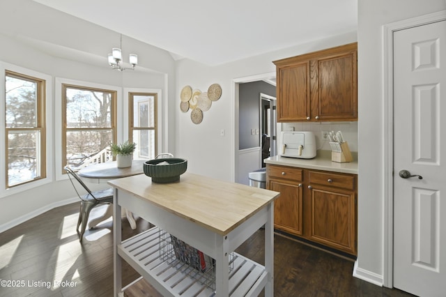 kitchen with light countertops, hanging light fixtures, backsplash, brown cabinets, and dark wood-style floors