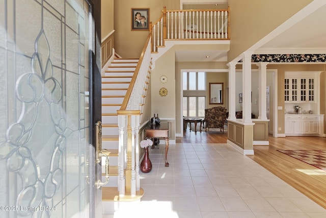 foyer featuring light tile patterned flooring, a towering ceiling, stairs, ornate columns, and crown molding