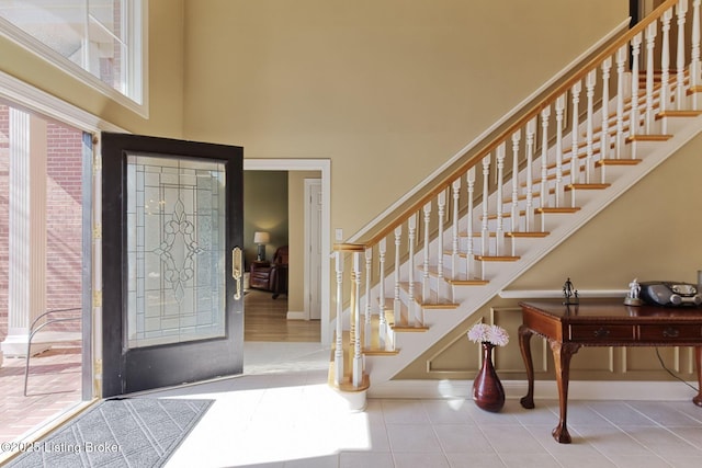 tiled foyer entrance with a towering ceiling, stairs, and baseboards