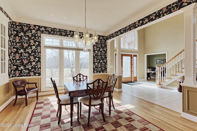 dining space with decorative columns, a wainscoted wall, stairway, ornamental molding, and a healthy amount of sunlight