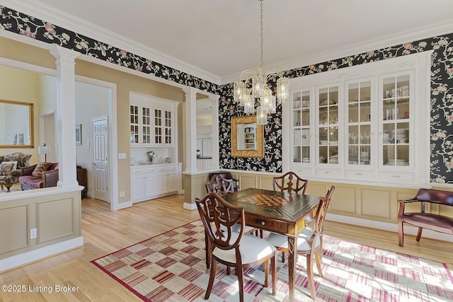 dining space with a notable chandelier, decorative columns, light wood-style flooring, and crown molding