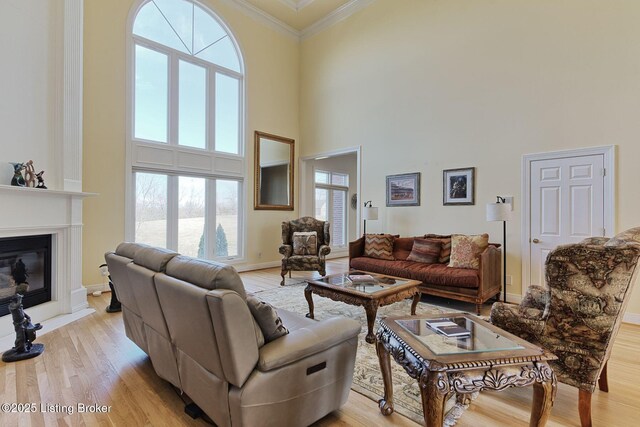 living room with baseboards, a glass covered fireplace, ornamental molding, a high ceiling, and light wood-style floors