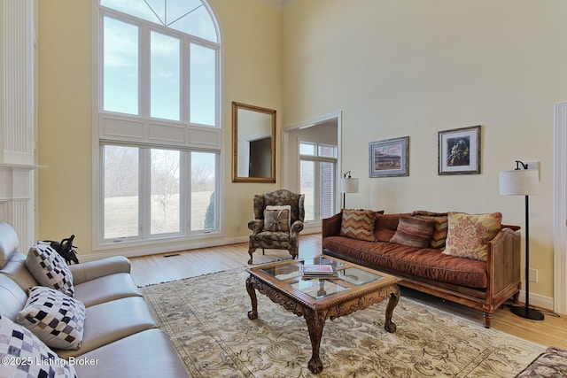 living room with a wealth of natural light, a towering ceiling, light wood-style flooring, and baseboards